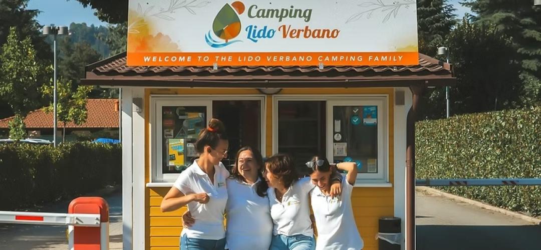 Quattro persone sorridenti davanti al colorato ingresso del Camping Lido Verbano.