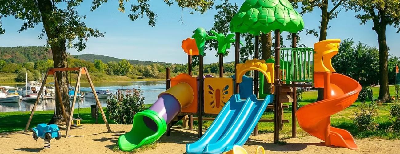Parco giochi colorato e vivace, scivoli e altalene vicino a un lago sereno.
