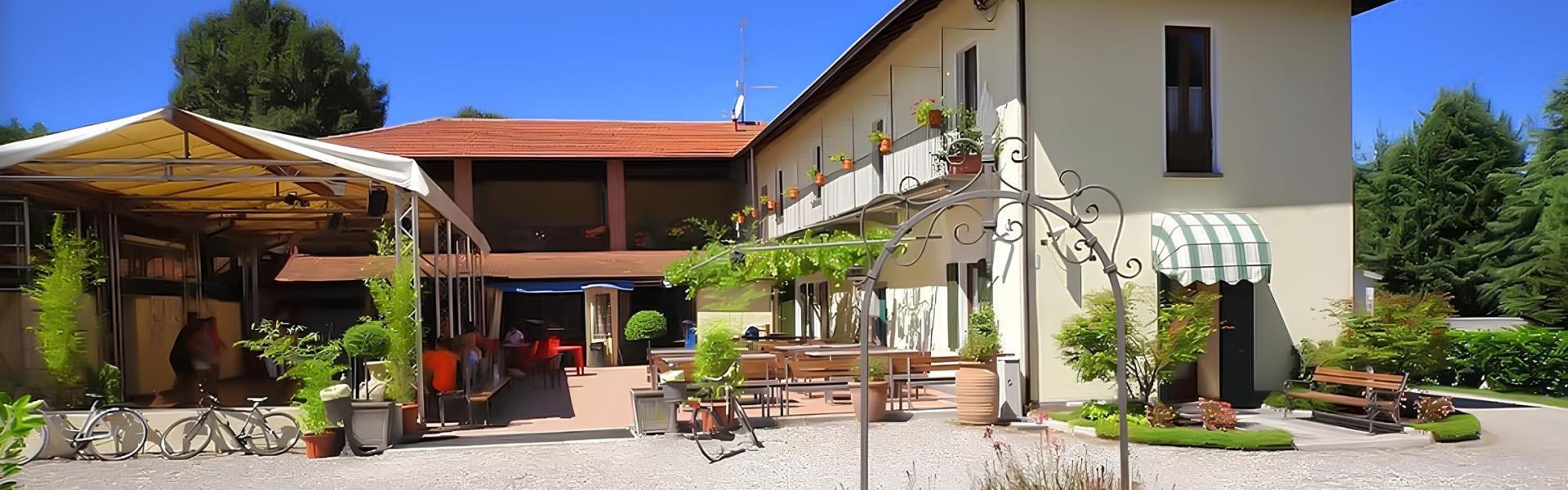 Cortile soleggiato con piante verdi, biciclette e tavoli all'aperto, atmosfera accogliente e serena.