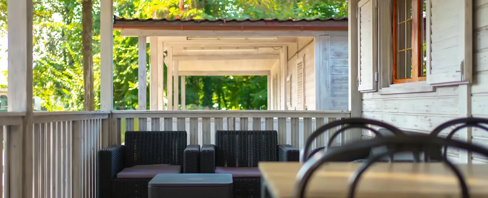 Veranda luminosa, arredi in vimini, atmosfera tranquilla tra natura verdeggiante e legno chiaro.