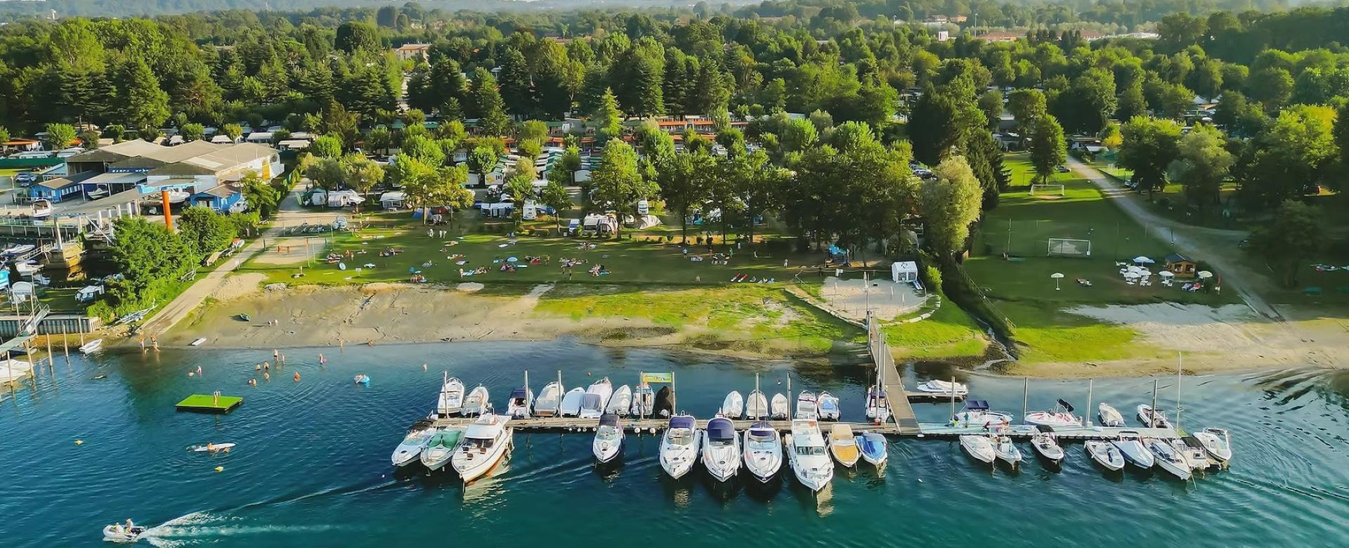 Porticciolo affollato, verde rigoglioso e persone che godono del sole su una spiaggia tranquilla.