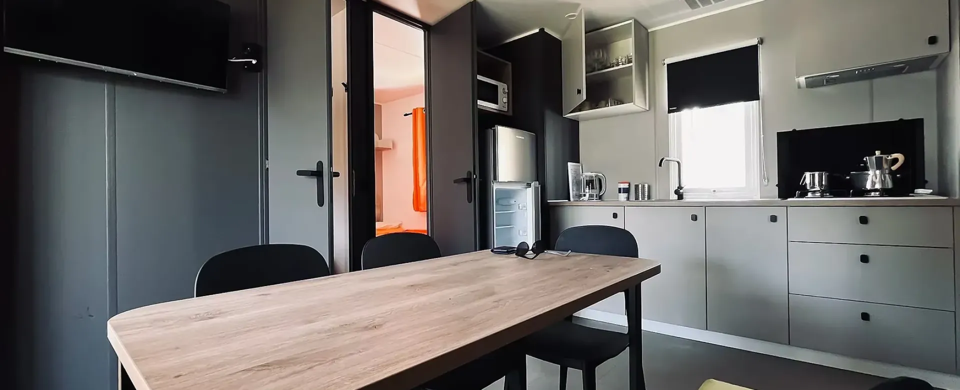 Cucina moderna, minimalista, con tavolo in legno e luce naturale filtrata da una finestra.