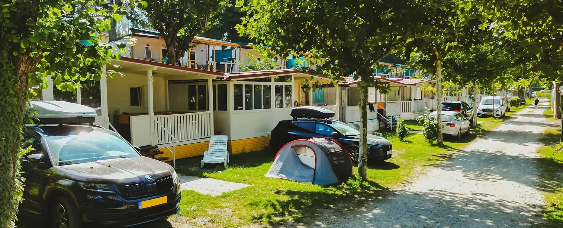 Campeggio estivo: bungalow, auto, tenda e alberi verdi sotto il sole.
