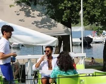 Momento rilassante al bar all'aperto, vista lago, conversazioni e sole estivo.