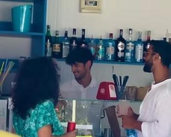 Persone sorridenti in un bar estivo, atmosfera rilassata e conviviale.