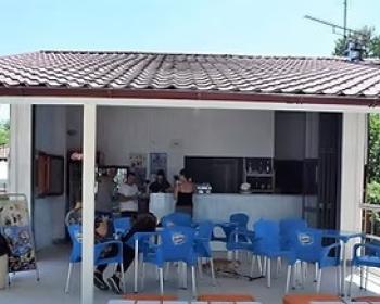 Bar esterno accogliente con sedie blu, tavoli bianchi e cuscini arancioni, atmosfera rilassante.