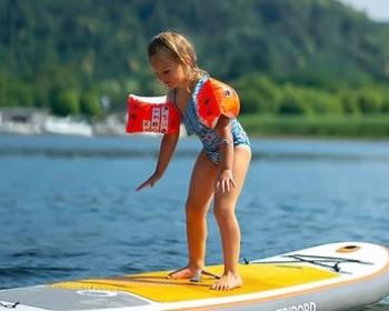 Bambina felice su paddleboard, con braccioli arancioni, esplora serena un lago estivo.