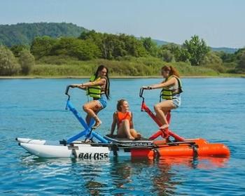 Tre persone in pedalò, sorridenti, godono del sole e dell'acqua in un paesaggio sereno.