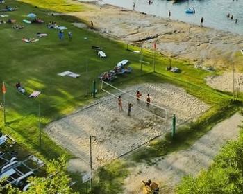 Spiaggia estiva, campo da beach volley, persone giocano e si rilassano al sole.