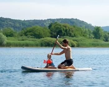 Padre e figlio sorridenti fanno paddle sul lago, circondati da natura rigogliosa.