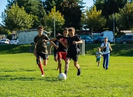 Ragazzi corrono su un campo verde, inseguendo un pallone, pieni di energia e gioia.