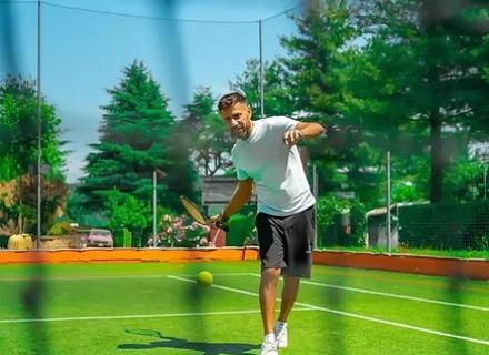 Uomo gioca a tennis all'aperto, energia e sole tra alberi verdi.