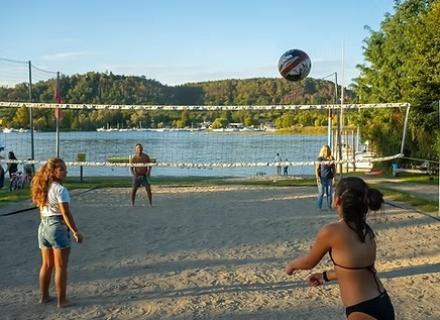 Giovani giocano a beach volley in riva al lago, atmosfera estiva e gioiosa.