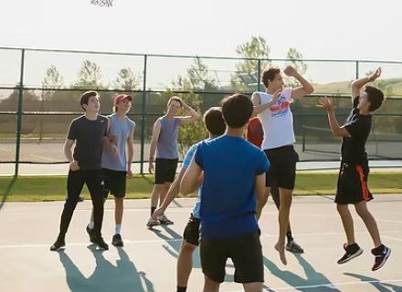Ragazzi giocano a basket all'aperto, energia e competizione sotto il sole estivo.