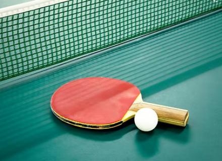 Racchetta da ping pong e pallina bianca su tavolo verde, pronte per la sfida.