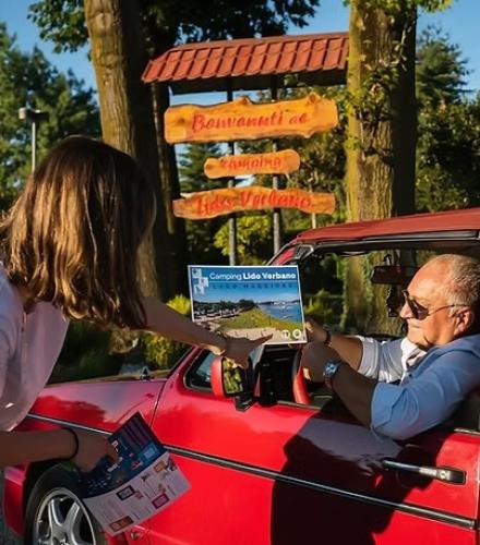 Un uomo in auto riceve un volantino al campeggio, atmosfera calda e accogliente.
