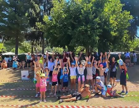 Gruppo di bambini felici al parco, braccia alzate, giornata soleggiata e gioiosa.