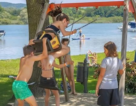 Bambini giocano felici sull'altalena vicino al lago, sole e risate estive.
