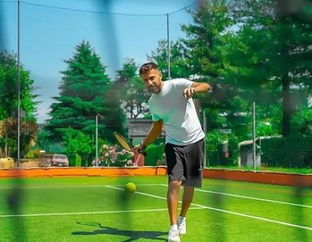 Uomo gioca a tennis all'aperto, energia e gioia sotto il sole estivo.