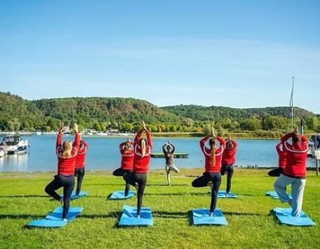 Gruppo fa yoga all'aperto vicino al lago, atmosfera serena e rilassante.