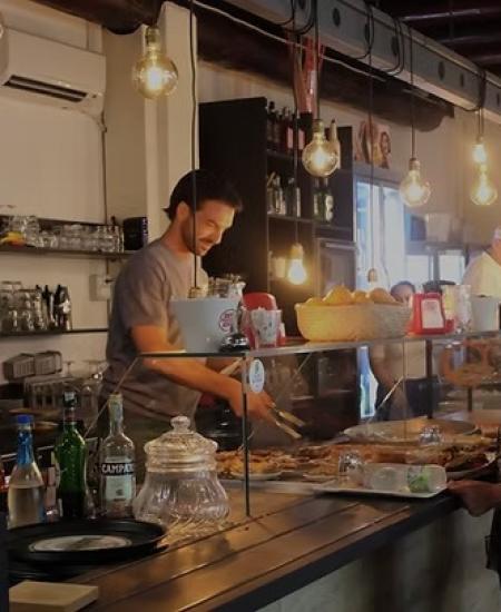 Ambiente accogliente, luci calde, barista sorridente serve cibo delizioso dietro il bancone.