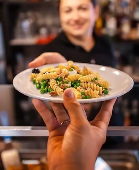 Un piatto di fusilli colorati viene servito con un sorriso caloroso e accogliente.