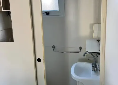 Bagno compatto, minimalista, con lavandino bianco e finestra che lascia entrare luce soffusa.