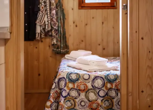 Accogliente stanza in legno, letto colorato, asciugamani morbidi, atmosfera calda e rilassante.