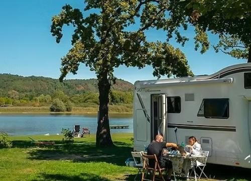 Camper vicino al lago, coppia felice pranza all'aperto, natura serena e rilassante.