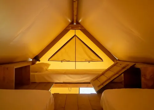 Interno di una tenda accogliente con letti, luce calda e atmosfera intima.