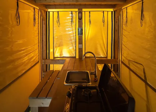 Interno di una tenda gialla, legno e luce calda creano un'atmosfera accogliente.