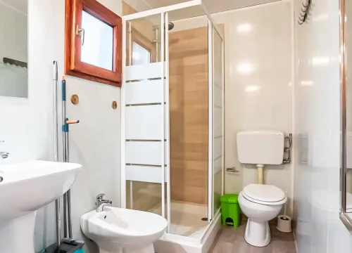 Bagno luminoso e ordinato, con doccia moderna, sanitari bianchi e pavimento in legno chiaro.
