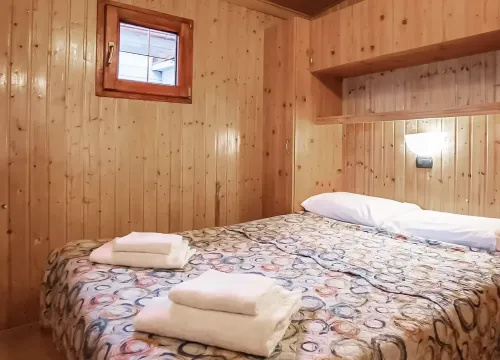 Accogliente camera in legno, letto matrimoniale con coperte colorate, atmosfera calda e intima.