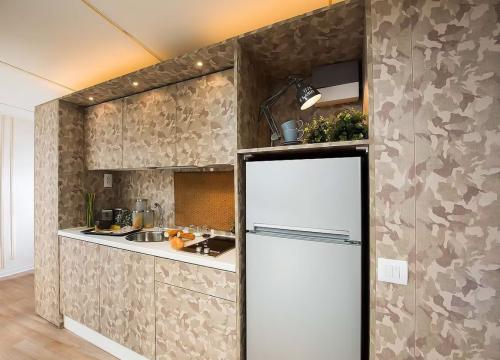 Cucina moderna con motivo mimetico, illuminazione calda, dettagli accoglienti e frigorifero argentato.
