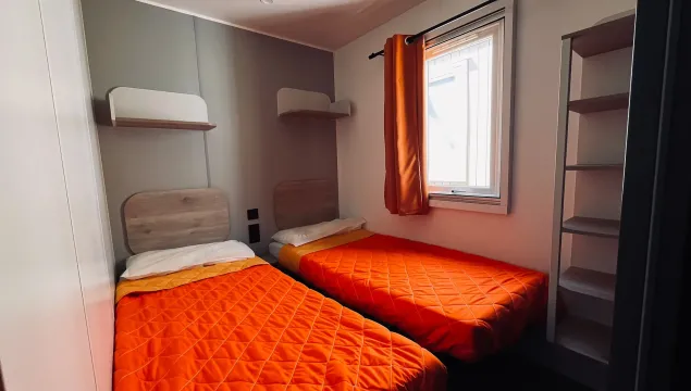 Camera accogliente con due letti singoli, coperte arancioni e luce calda dalla finestra.