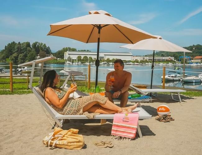 Coppia rilassata in spiaggia, sotto ombrelloni, con drink, atmosfera serena e soleggiata.
