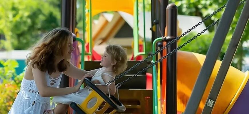 Madre e figlia sorridono insieme su un'altalena in un parco giochi colorato.