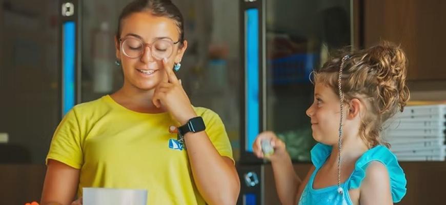 Due bambine sorridenti, una indica il viso, l'altra osserva curiosa e felice.